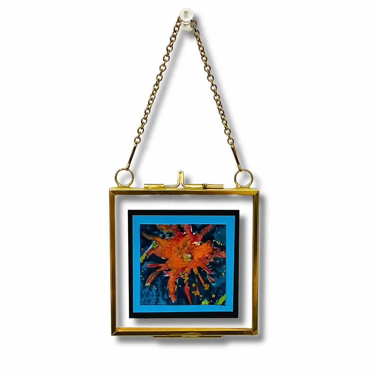red bloom on a blue background in a gold floating frame with a gold chain
