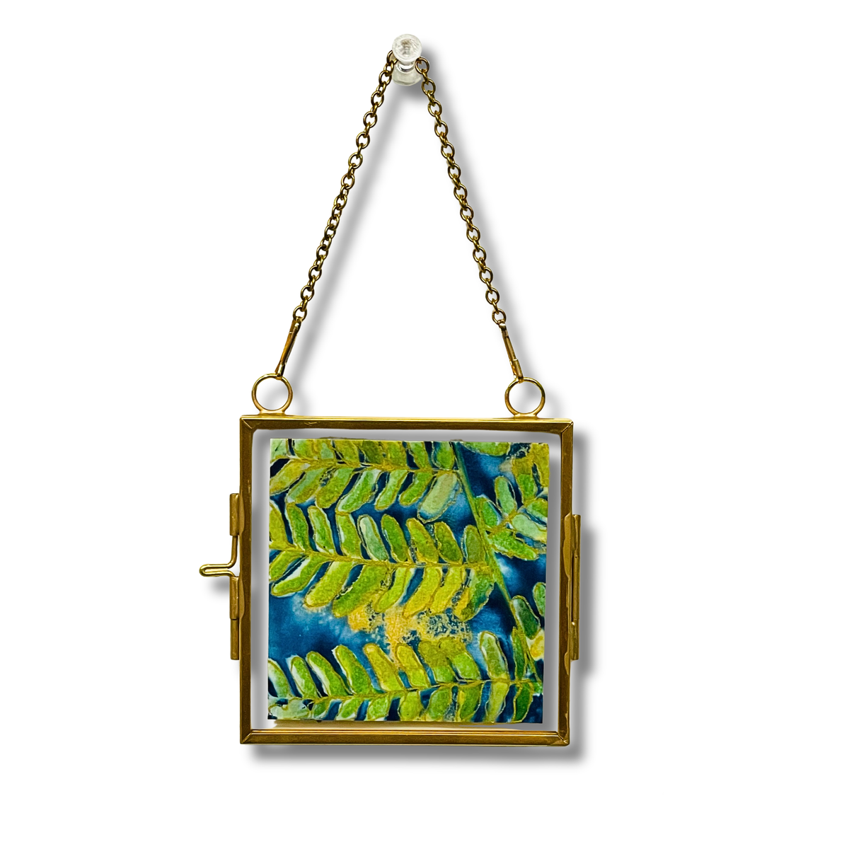Green and gold fern on blue background in a gold metal frame with a chain