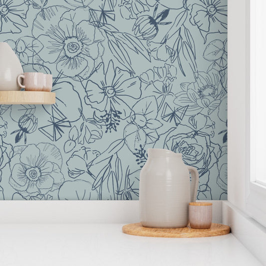 Pale blue botanical wallpaper with dark floral line drawings above a white countertop styled with ceramic pottery.