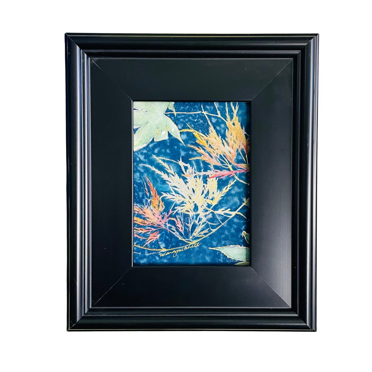A black wooden picture frame with a wide mat border, showcasing a blue and orange autumn maple leaf print, set against a plain white background.