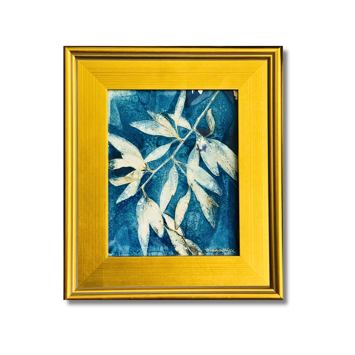 A framed botanical art print featuring white and light blue willow oak leaves on a textured blue background, enclosed in a wide gold frame against a white background.