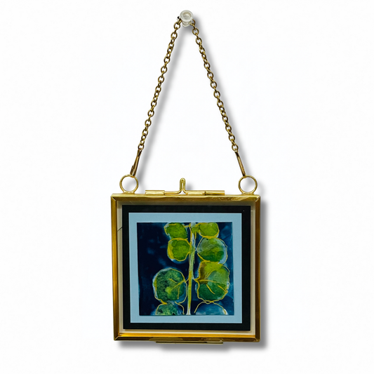 A square gold-tone clutch bag with a hinged clasp and hanging chain, featuring a printed botanical design of green leaves on a dark blue background.
