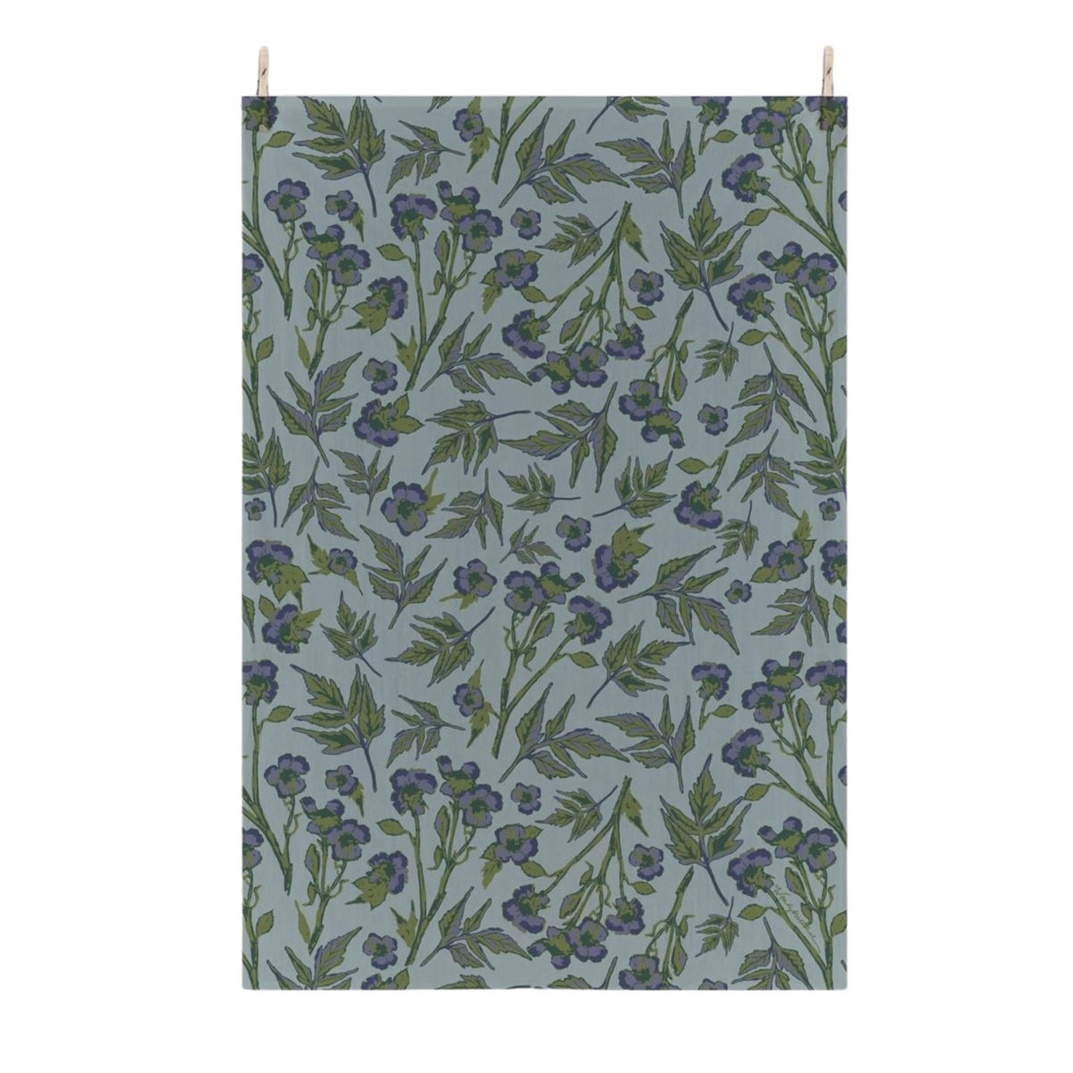 A flour sack tea towel with a botanical pattern of blue roses and green leaves on a muted blue-gray background, suspended by two small wooden pegs against a plain white wall.