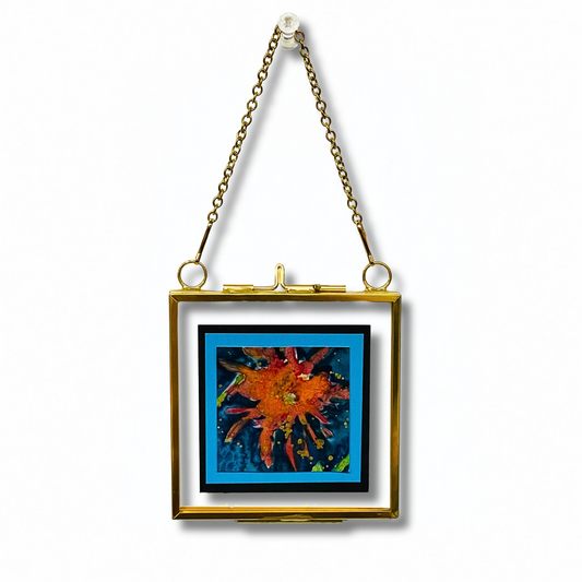 red bloom on a blue background in a gold floating frame with a gold chain