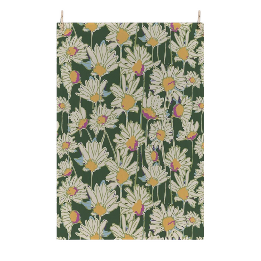 A rectangular flour sack tea towel with a repeating daisy floral pattern on a dark green background, suspended by two small wooden dowels against a plain white wall.