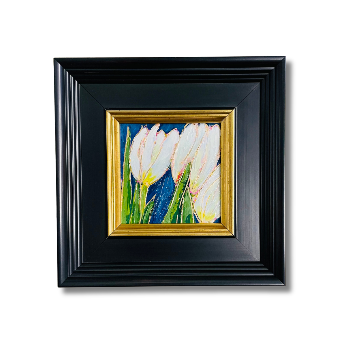 A framed painting of white tulips with green stems on a dark blue background, set in a black frame with a gold inner border, shown against a plain white background.