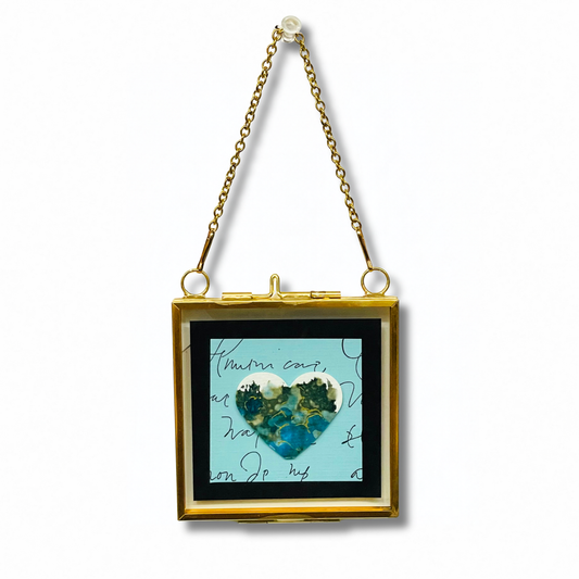 Heart shape on a light blue background with handwriting. In a gold metal frame with a chain