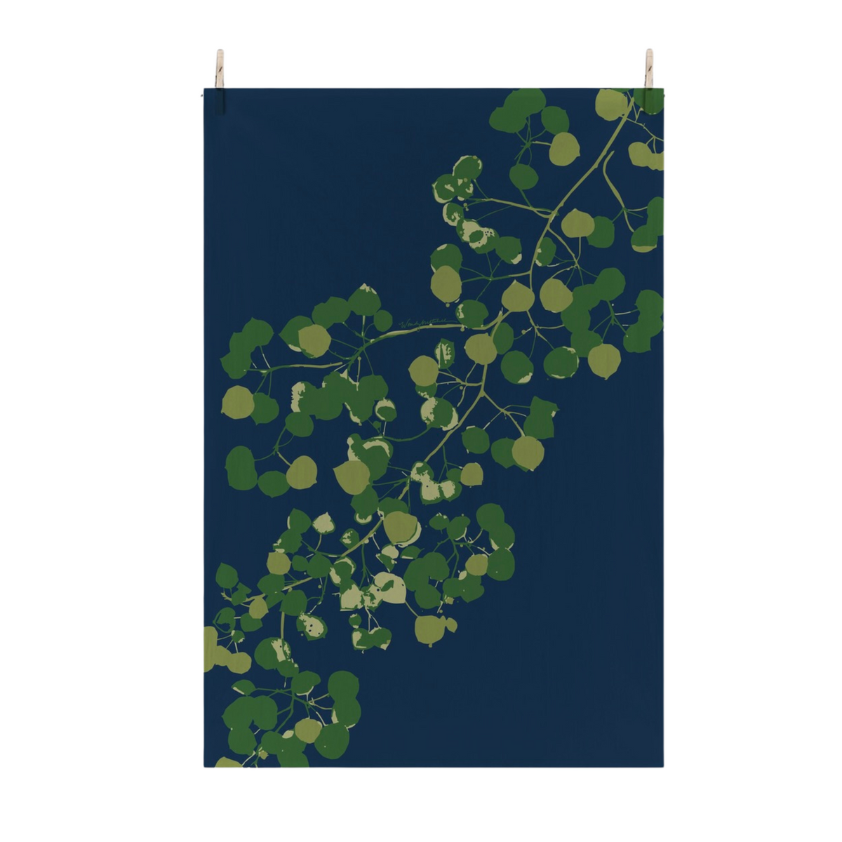 A vertical flour sack tea towel with a dark navy blue background and a stylized green aspen leaves, suspended by two small wooden pegs against a plain white wall.