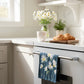 Navy Blue towel with white daisies on a  Flour Sack Tea Towel hanging on an oven door in a kitchen.