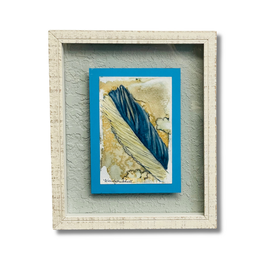 Framed abstract art print featuring a textured feather design in deep blue and beige tones, set within a distressed off-white wooden frame against a light gray background.
