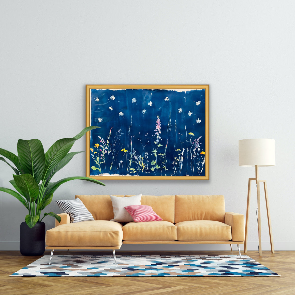 A framed abstract floral painting in deep blue with white and yellow wildflower-like shapes, hung on a light gray wall above a mustard yellow sofa in a styled living room with a plant, floor lamp, and patterned rug.
