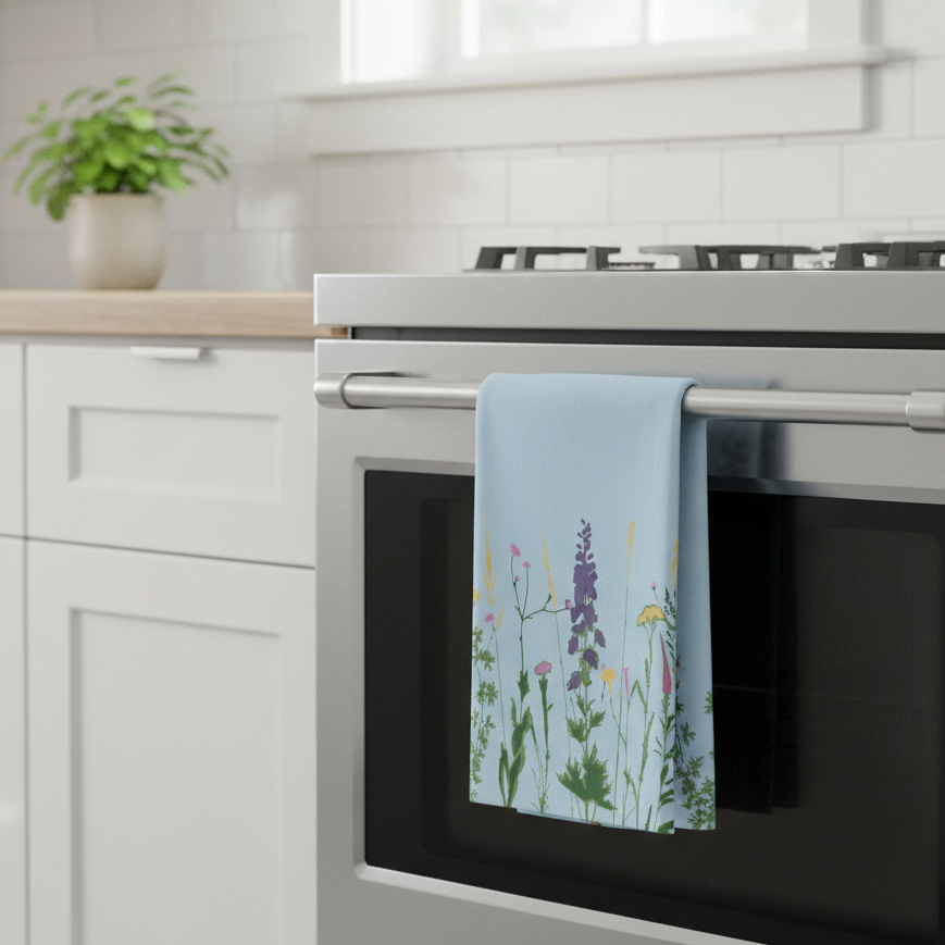 A light blue kitchen towel with a colorful wildflower print hangs from the stainless steel handle of a built-in oven in a bright, modern kitchen.